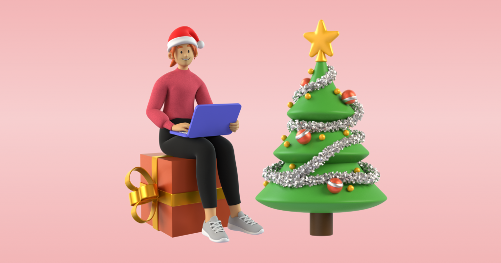 Kvinne i raud gensar og nisselue sit på ein stor pakke, med laptop på fanget. Juletre ved sidan av.
