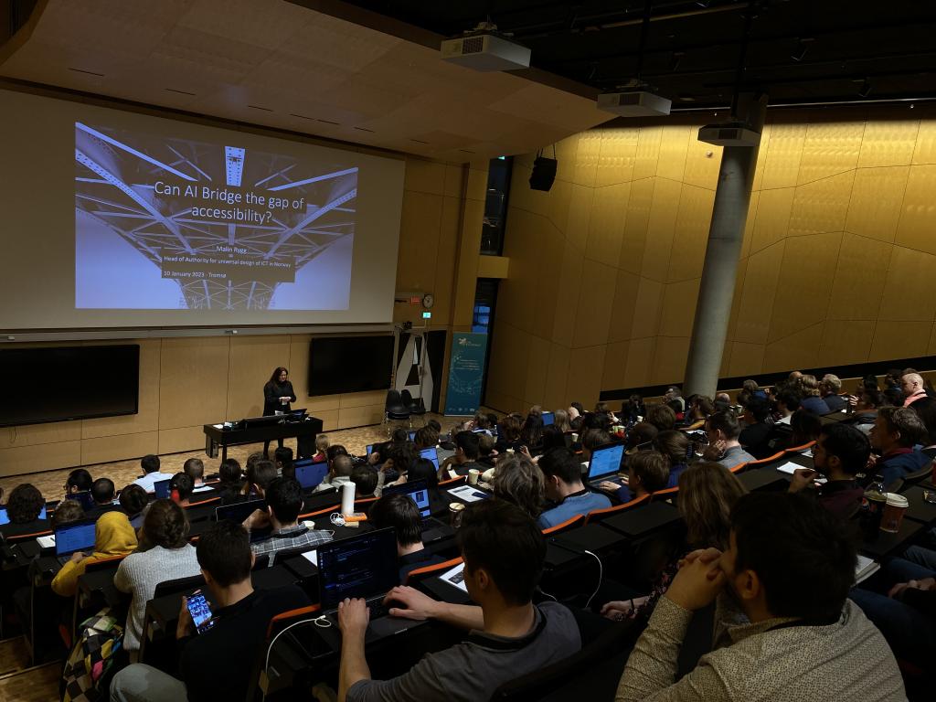 Malin Rygg is giving a speech at the NLDL conference in a packed hall at the university of Tromsø. She is showing her presentation on a big screen behind her.