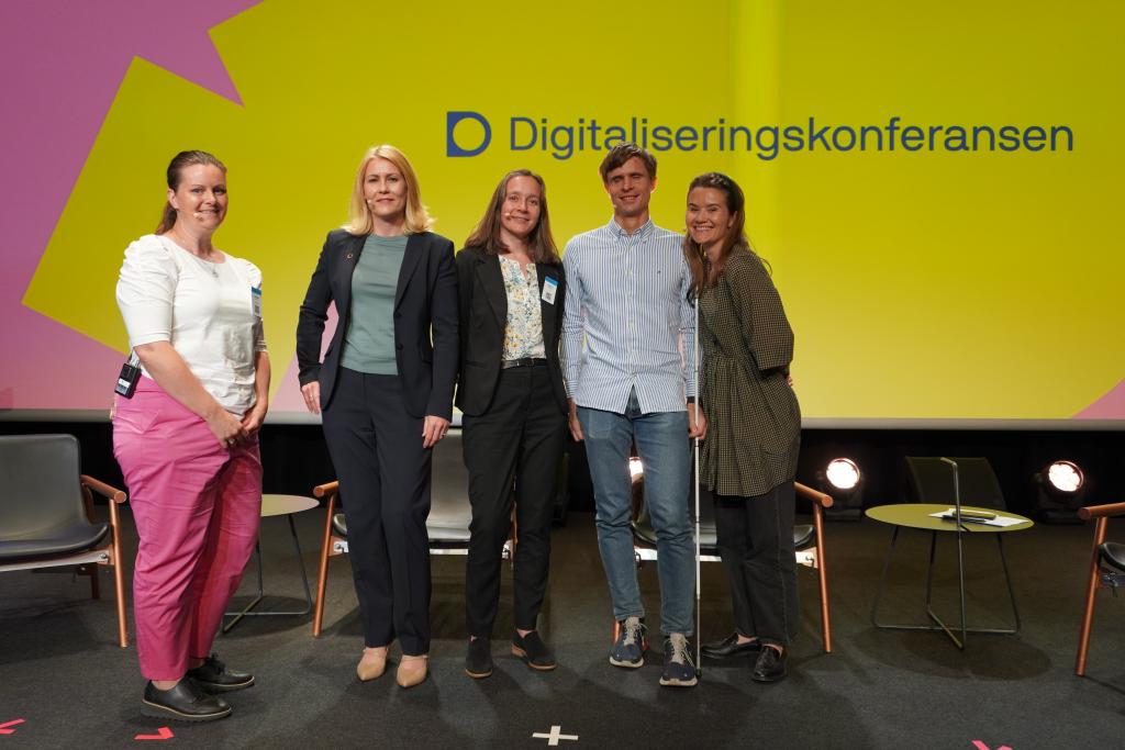 Bilde av inkluderingsrådet som står sammen og smiler til kamera. Fra venstre: Camilla Stolp, Kristine Dahl Steidel, Heidrun Reisæter, Kristoffer Lium og Live Nelvik. I bakgrunnen står teksten "Digitaliseringskonferansen" på storskjerm.