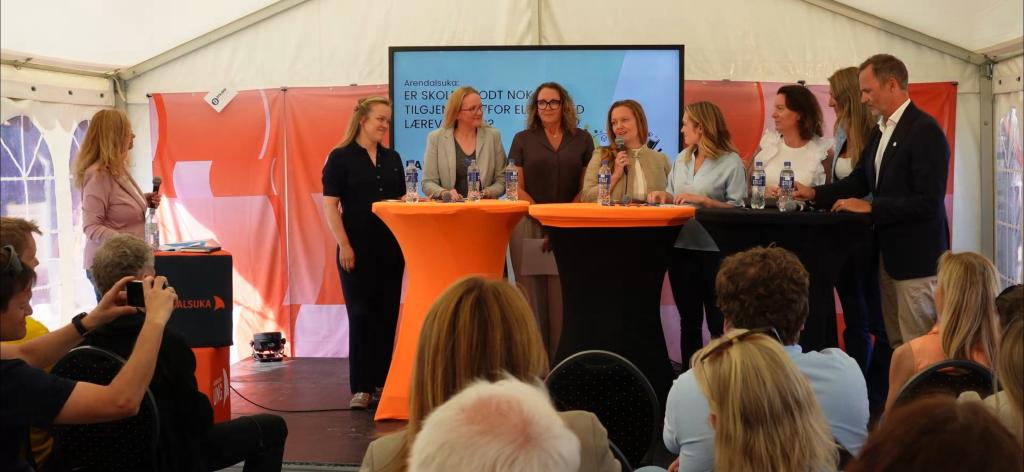 Ni personar på scena i debatt under Arendalsveka, inkludert ordstyraren heilt til venstre. Bilde tatt frå bak i teltet, med ryggen til publikum i forgrunnen.